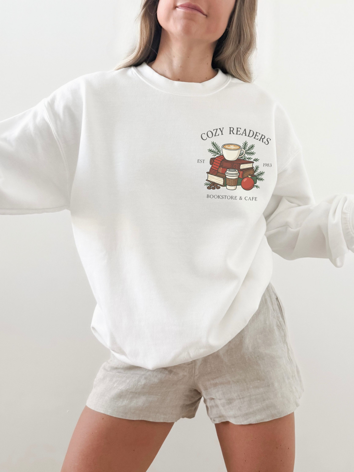 girl standing wearing a white sweatshirt with a small cozy readers coffee shop graphic on the front chest