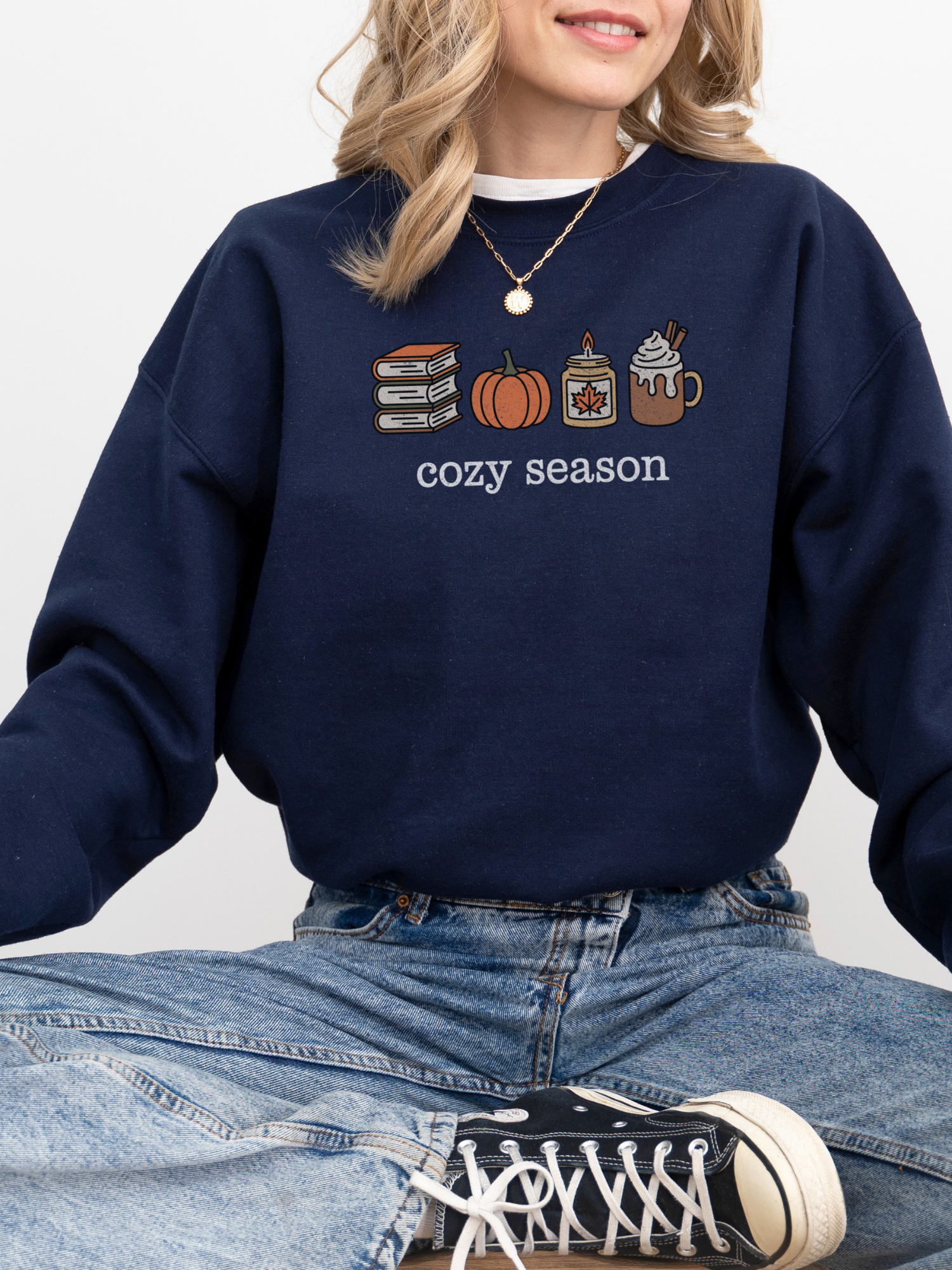 girl sitting in navy sweatshirt with cozy season fall icons including pumpkin, books, and coffee
