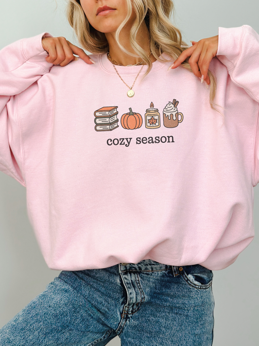 girl wearing light pink sweatshirt with cozy season icons including books, pumpkin, candle, and coffee