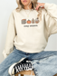 Sand: girl sitting in sand sweatshirt with cozy season print showing books, fall candle, pumpkin, and whipped drink
