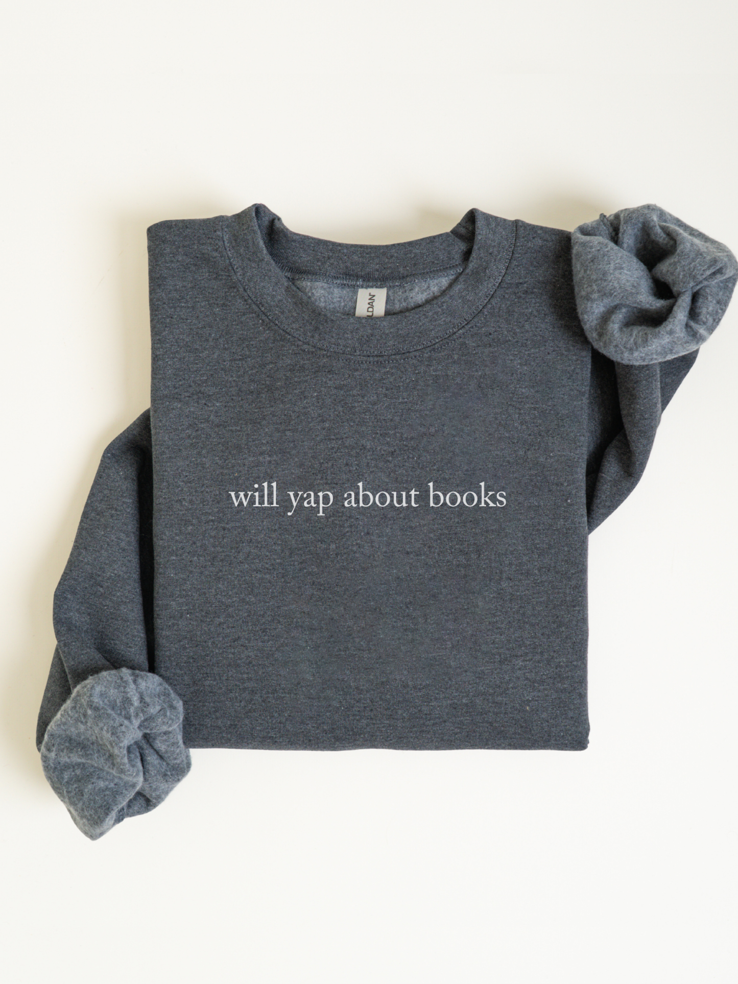 Folded dark heather grey sweatshirt with will yap about books printed in white text styled in a clean flat lay with sleeves rolled inward on a light background