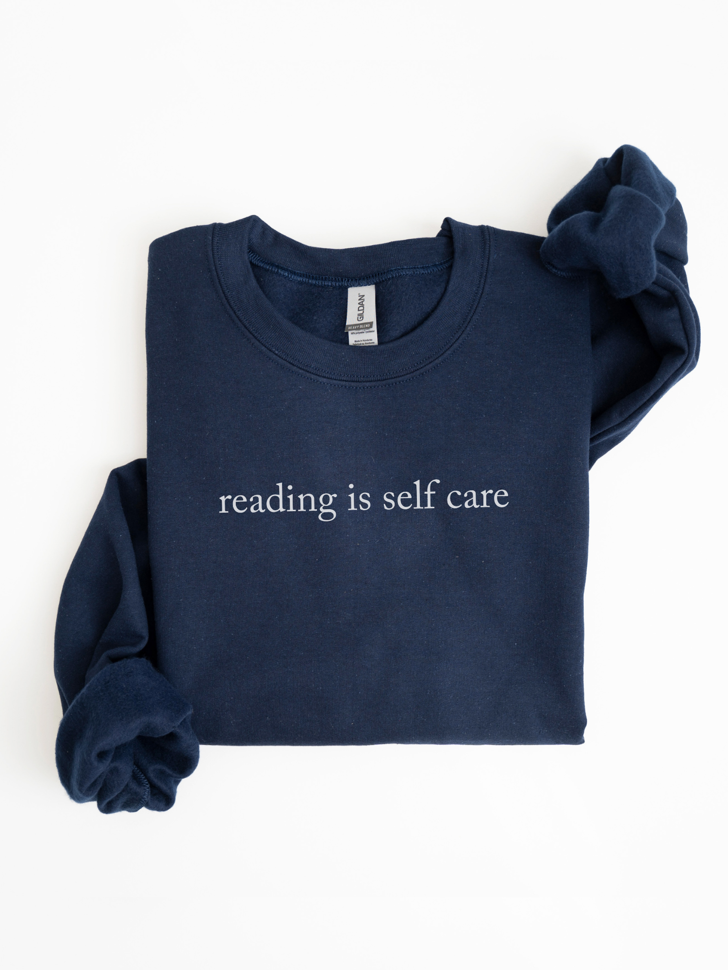 Folded navy blue sweatshirt with reading is self care printed in white text styled in a clean flat lay against a white background with sleeves slightly tucked