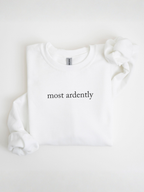 Folded white sweatshirt featuring most ardently in black text displayed in a bright flat lay setup with sleeves folded inward on a neutral background