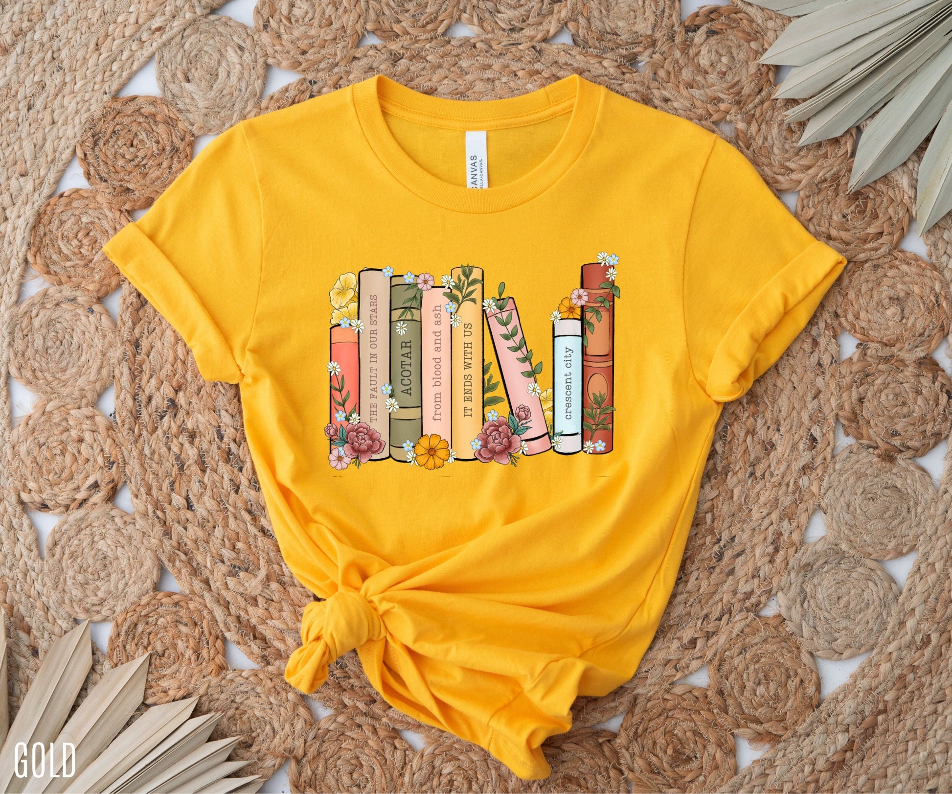 flatlay of gold t-shirt with custom book shelf graphic featuring pastel flowers and titles