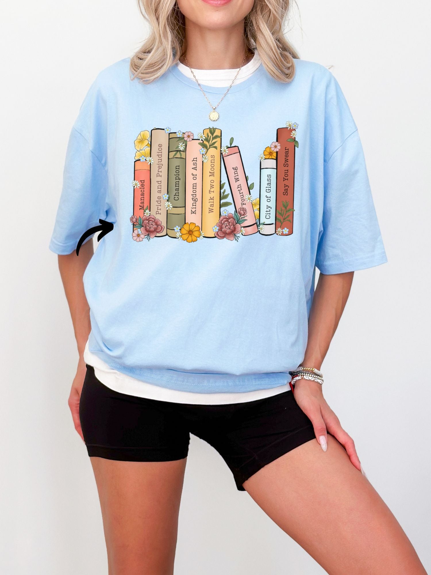 woman wearing light blue shirt with colorful custom book stack graphic and flower details