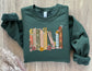 folded forest green sweatshirt with floral illustrated book spines including The Book Thief and A Court of Mist and Fury
