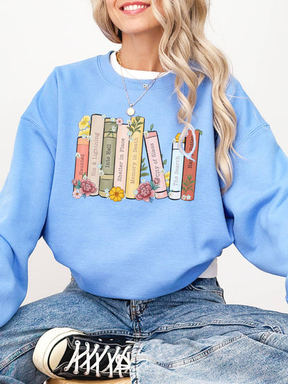 woman wearing light blue sweatshirt with colorful book stack including Haunting Adeline, Sky Without Stars, and Divergent