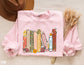 folded pink sweatshirt with pastel book spine design featuring floral fantasy titles like ACOTAR and Fourth Wing