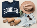 folded navy sweatshirt with bold white varsity-style BOOKISH text, styled with tan hat, sunglasses, and denim shorts