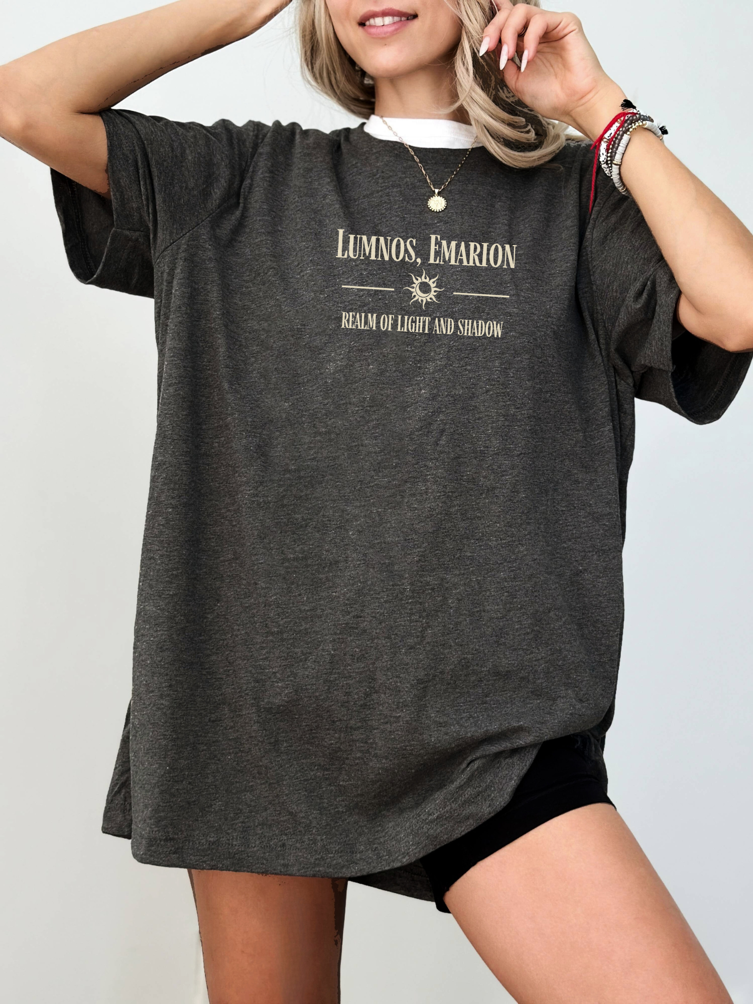 Oversized dark grey heather shirt with off-white print featuring the words "Lumnos, Emarion - Realm of Light and Shadow", styled with layered necklaces and black biker shorts

