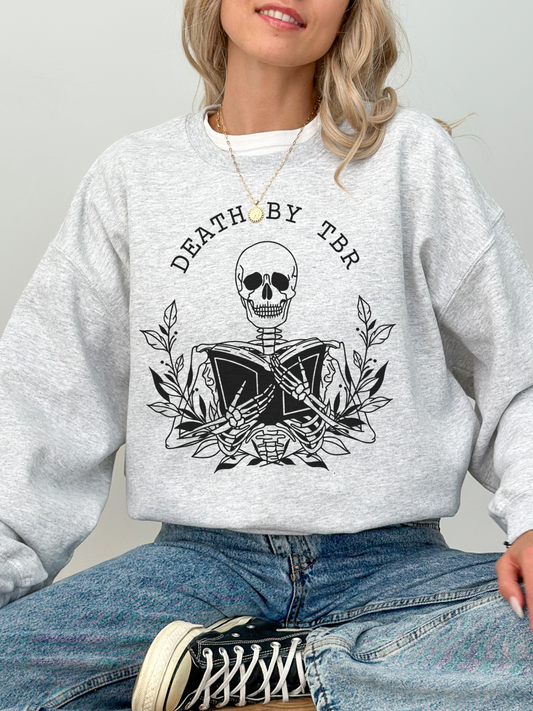 woman wearing ash grey Death by TBR sweatshirt with skeleton reading books, styled with jeans