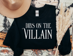 flat lay of black Dibs on the Villain sweatshirt styled with hat, book, and pampas grass