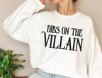 woman in oversized white sweatshirt with bold black Dibs on the Villain text, styled casually
