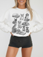 smiling model in white dog and books sweatshirt with corgi, retriever, and bulldog illustrations stacked on classic books