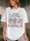 A woman wearing an oversized white graphic t-shirt with a Halloween-themed design featuring skeletons reading and the text 'dying to read my BOOK'.