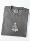A folded pepper t-shirt with an embroidered white graphic of a skeleton reading a book on the front, styled with a silver chain necklace featuring a small round pendant, on a white background.
