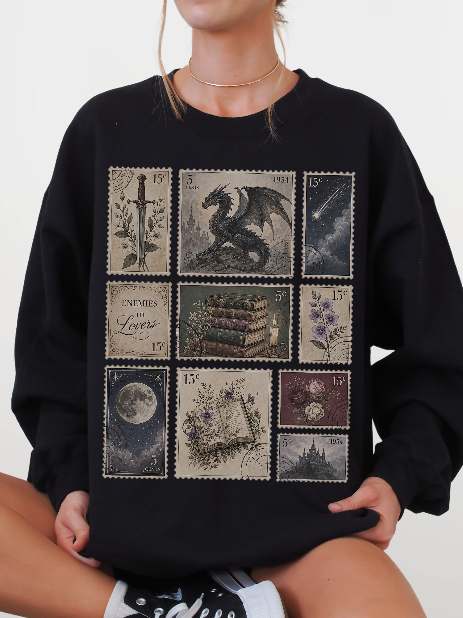 Woman wearing black sweatshirt with fantasy postage stamp collage featuring enemies to lovers text dragon moon books flowers and gothic fantasy castle artwork