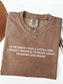 A folded espresso brown t-shirt with white text that reads 'EVER SINCE I WAS A LITTLE GIRL I KNEW I WANTED TO READ ABOUT DRAGONS AND MAGIC'. A silver necklace with a gold charm is draped over the collar.