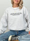 A woman wearing an ash heather gray crewneck sweatshirt with black text that reads 'EVER SINCE I WAS A LITTLE GIRL, I KNEW I WANTED TO READ ABOUT DRAGONS AND MAGIC'. She is also wearing blue jeans and a black and white canvas sneaker.