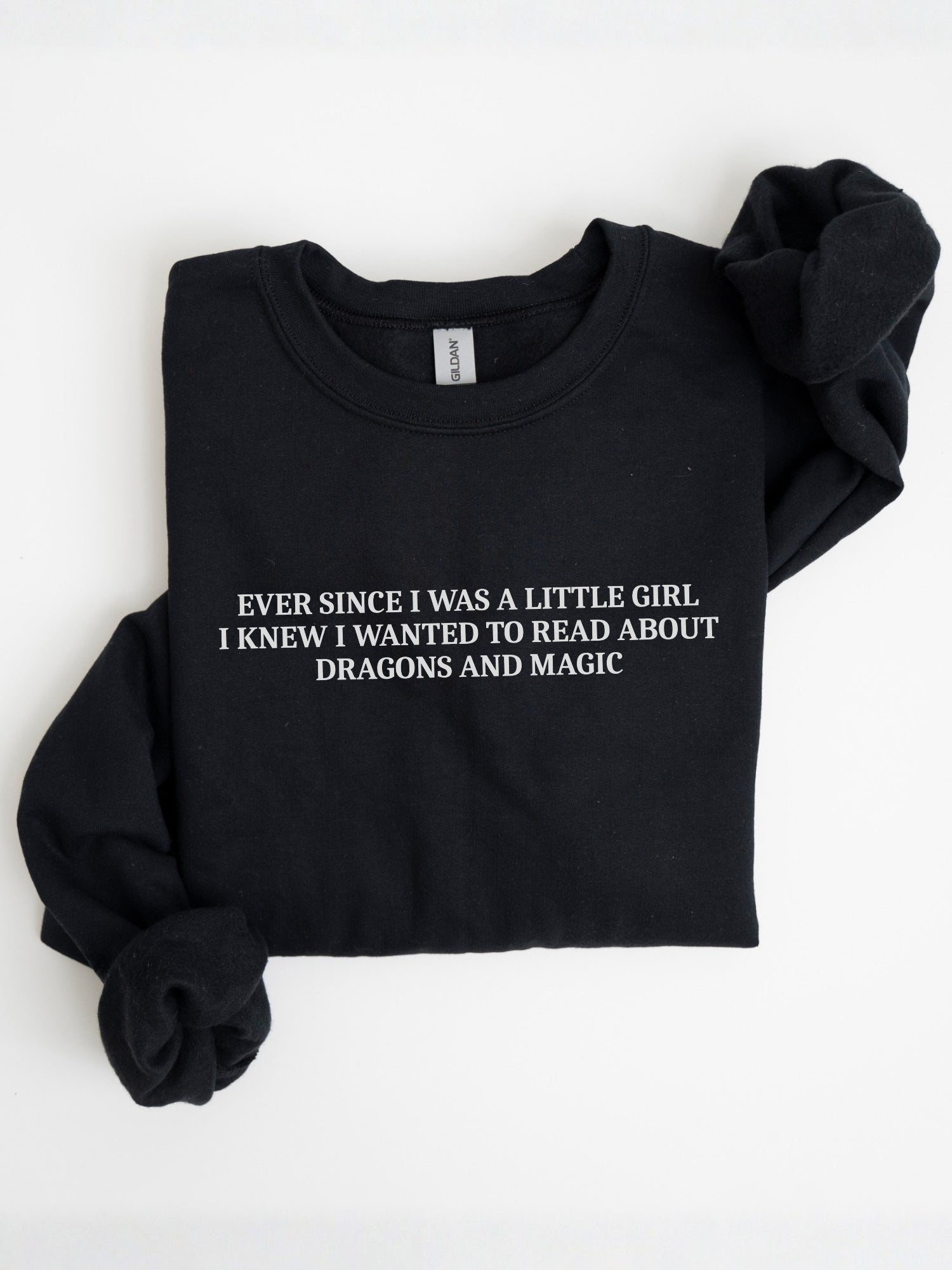 A folded black fantasy reader sweatshirt with “Ever Since I Was a Little Girl I Knew I Wanted to Read About Dragons and Magic”