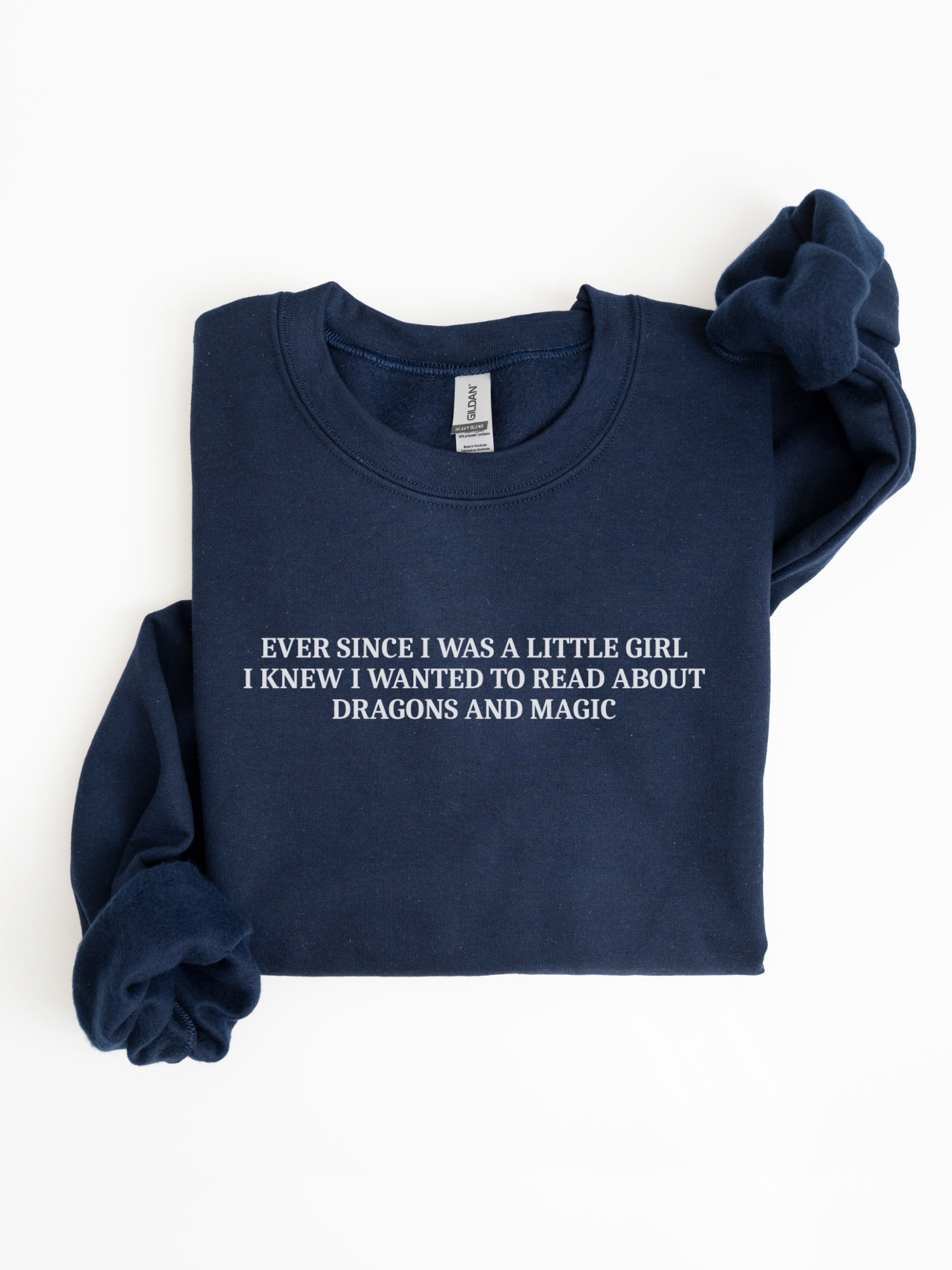 A navy blue sweatshirt with white printed text on the chest reading 'EVER SINCE I WAS A LITTLE GIRL, I KNEW I WANTED TO READ ABOUT DRAGONS AND MAGIC', shown folded on a white background.