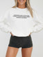 A woman wearing a white crewneck sweatshirt with black text that reads 'EVER SINCE I WAS A LITTLE GIRL, I KNEW I WANTED TO READ ABOUT DRAGONS AND MAGIC', paired with black shorts, against a plain light gray background.