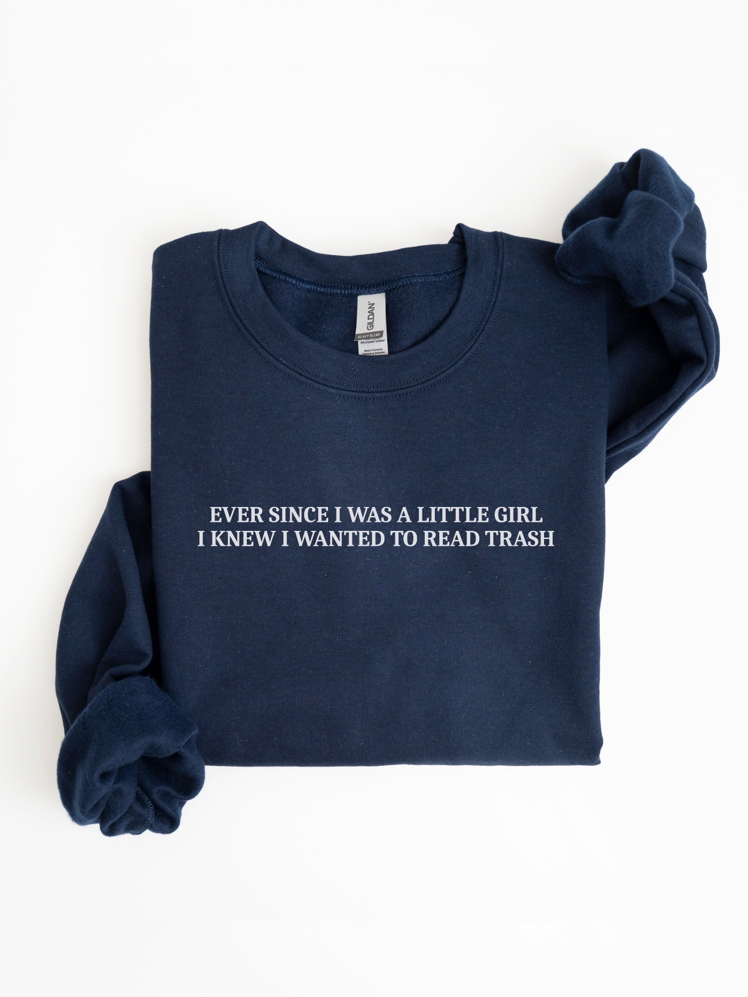 A navy blue folded crewneck sweatshirt with white text reading 'EVER SINCE I WAS A LITTLE GIRL. I KNEW I WANTED TO READ TRASH' on the chest, displayed on a clean white background.