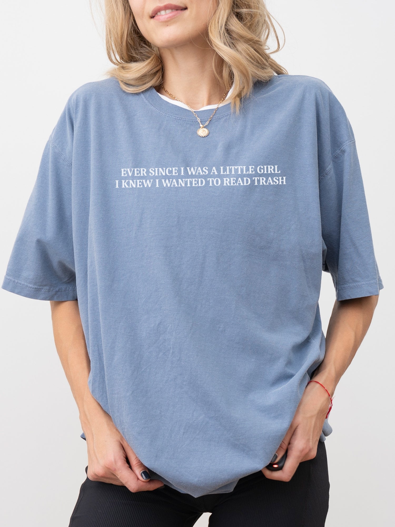 A woman wearing an oversized blue jean t-shirt with funny “Ever Since I Was a Little Girl I Knew I Wanted to Read Trash” quote