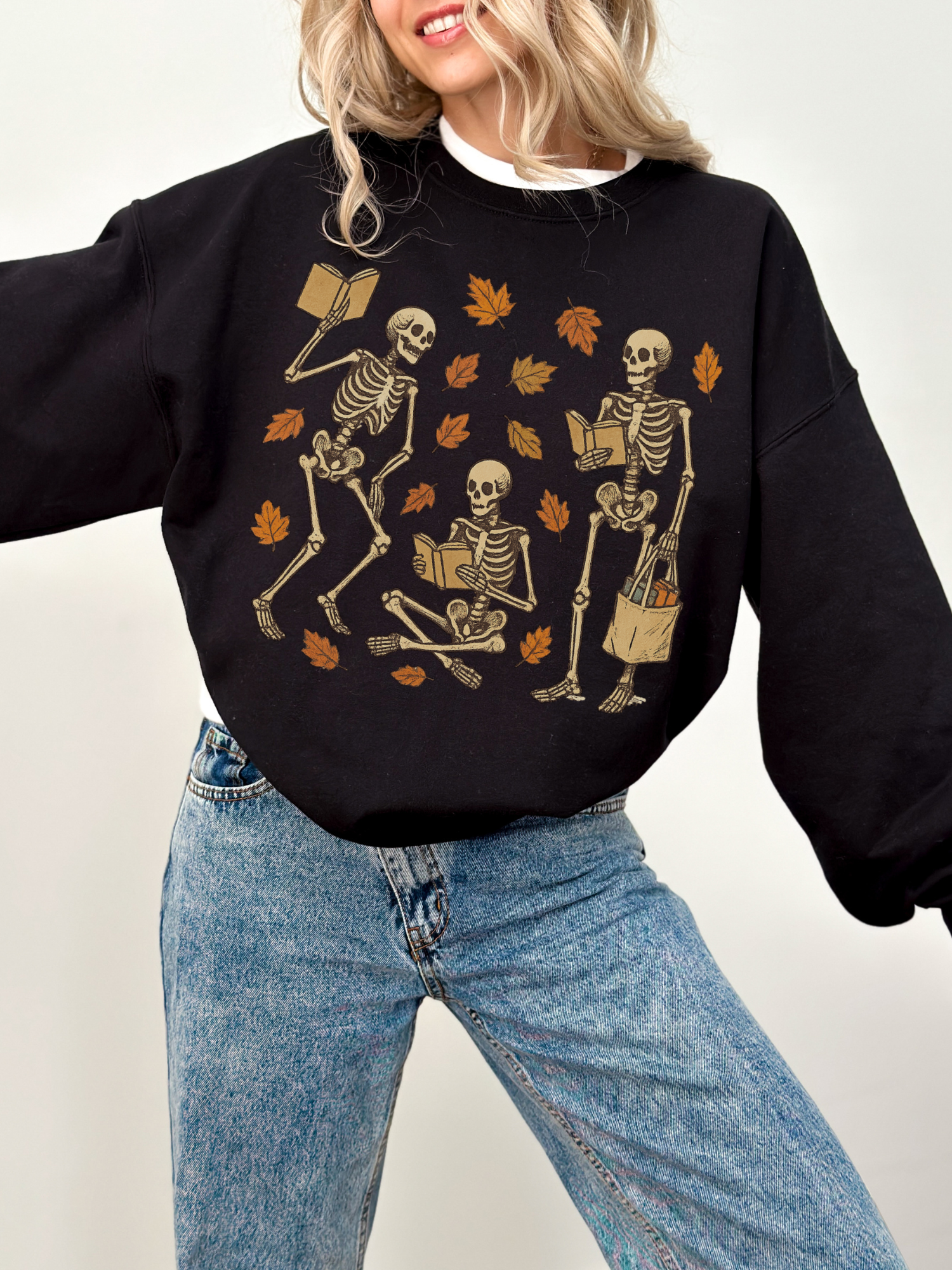 Black sweatshirt with whimsical skeleton reading illustration, styled with light-wash jeans and a cheerful expression