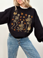 Black sweatshirt with whimsical skeleton reading illustration, styled with light-wash jeans and a cheerful expression