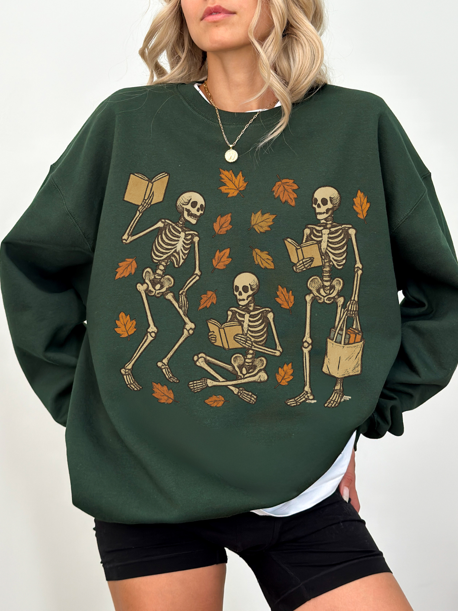 Forest green sweatshirt with vintage-style skeletons and fall leaves, worn by woman with black shorts and layered tee