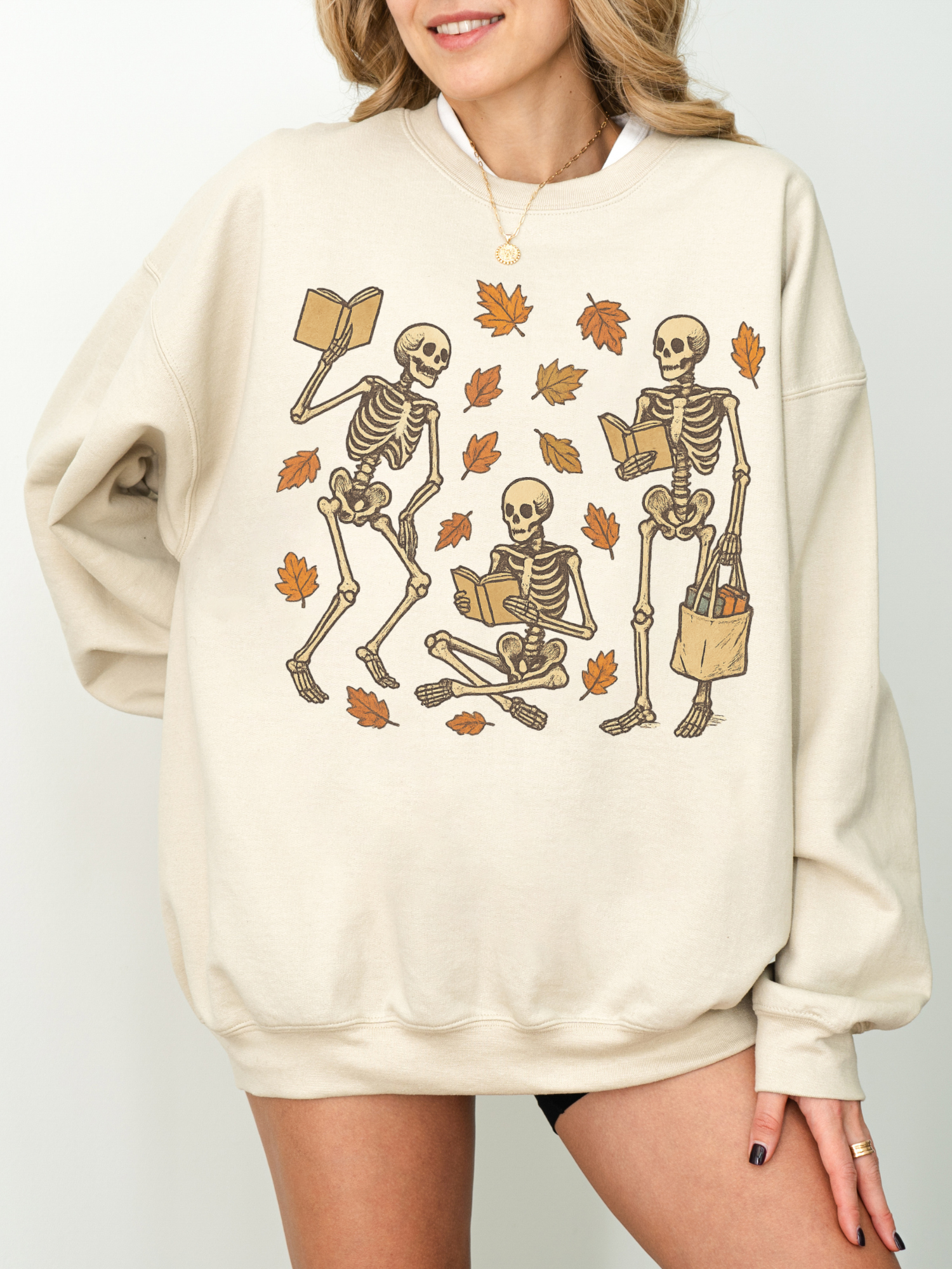 Neutral sand-colored sweatshirt with skeleton fall reading scene, modeled with a smile and relaxed hands