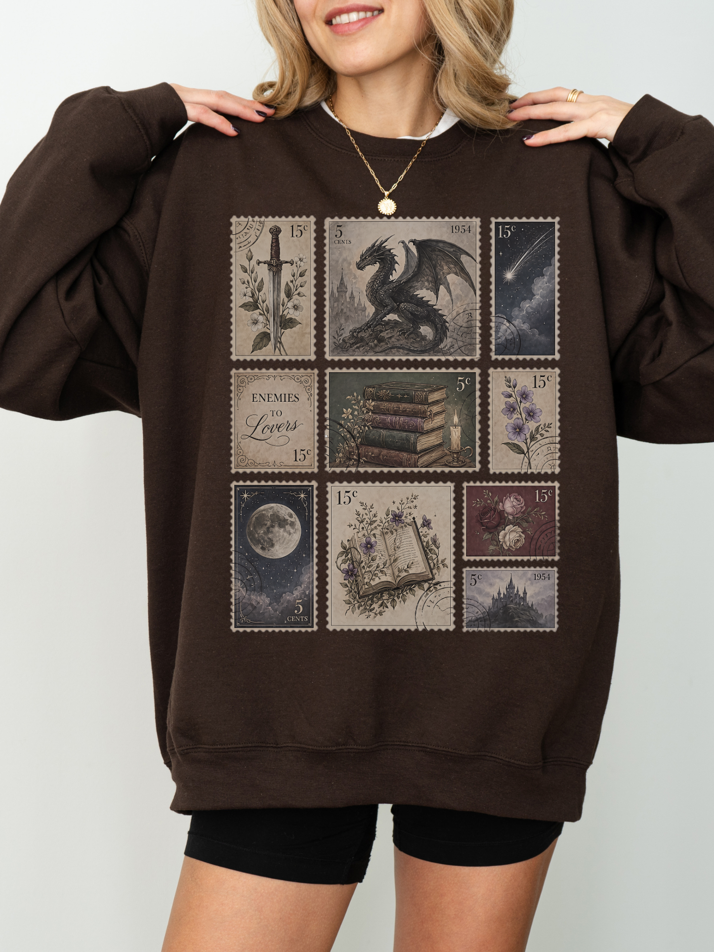Woman wearing brown oversized sweatshirt with vintage fantasy stamp collage featuring dragon sword books moon floral art and enemies to lovers inspired design