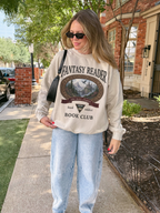 woman wearing a sand Fantasy Reader Book Club sweatshirt featuring a fantasy landscape, castle, dragon, and one more chapter graphic for romantasy readers