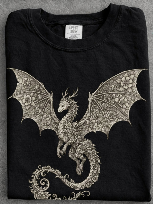 A folded black crewneck t-shirt featuring a highly detailed, ornate silver-gray dragon graphic with intricate floral patterns on its wings and tail, displayed on a neutral gray background.