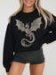 A woman wearing a black crewneck sweatshirt with a large silver dragon graphic on the front, paired with black shorts, against a plain white background.