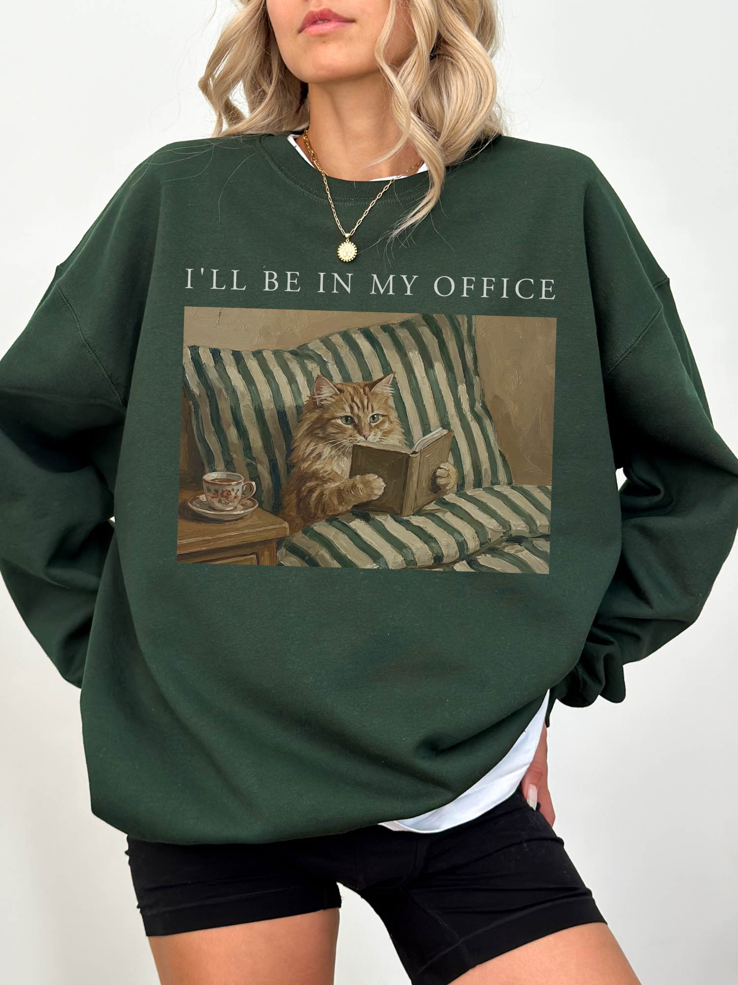 Dark green oversized sweatshirt with Ill be in my office text and a cozy cat reading in bed illustration. Styled as a relaxed casual outfit for readers, introverts, and cat lovers who enjoy cozy apparel.