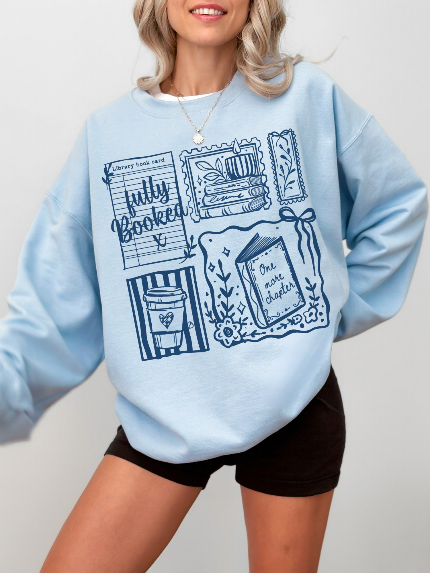 model wearing light blue fully booked book lover sweatshirt with cozy reading graphics styled casually with shorts