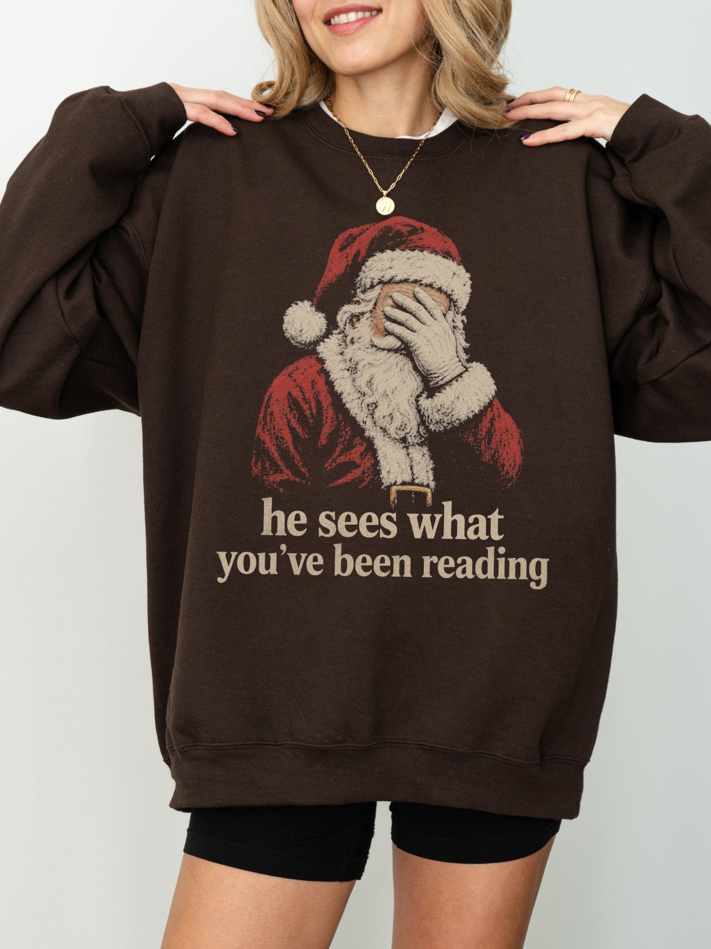 Dark Chocolate Gildan sweatshirt with vintage Santa covering his eyes and he sees what you’ve been reading text, a funny Christmas book lover sweatshirt for readers