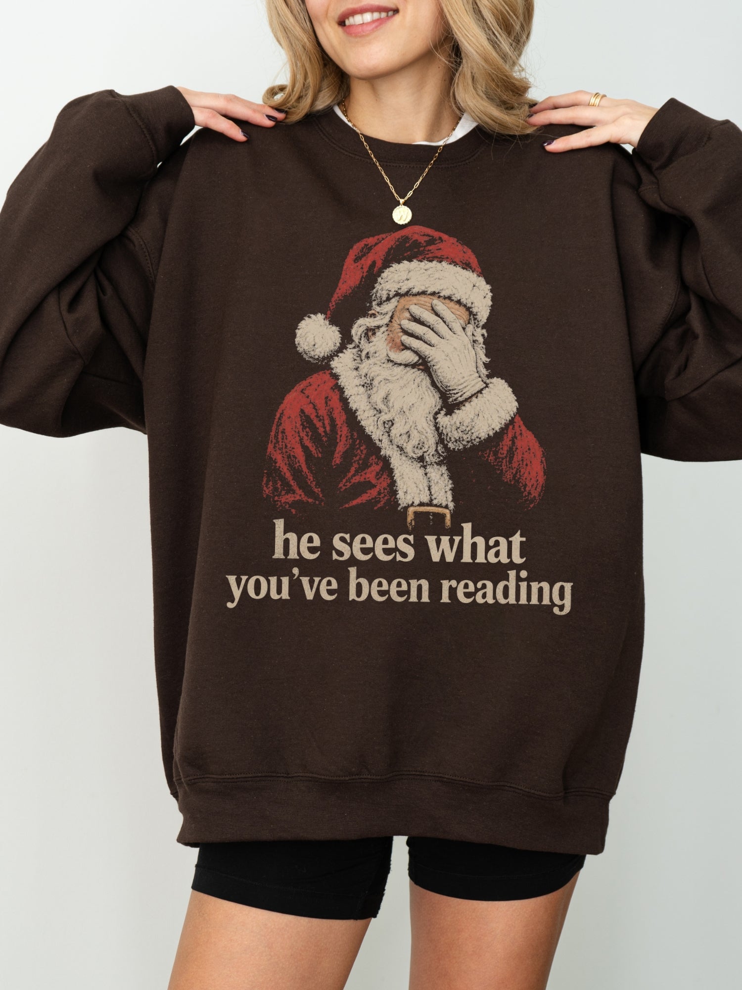 Dark Chocolate Gildan sweatshirt with vintage Santa covering his eyes and he sees what you’ve been reading text, a funny Christmas book lover sweatshirt for readers