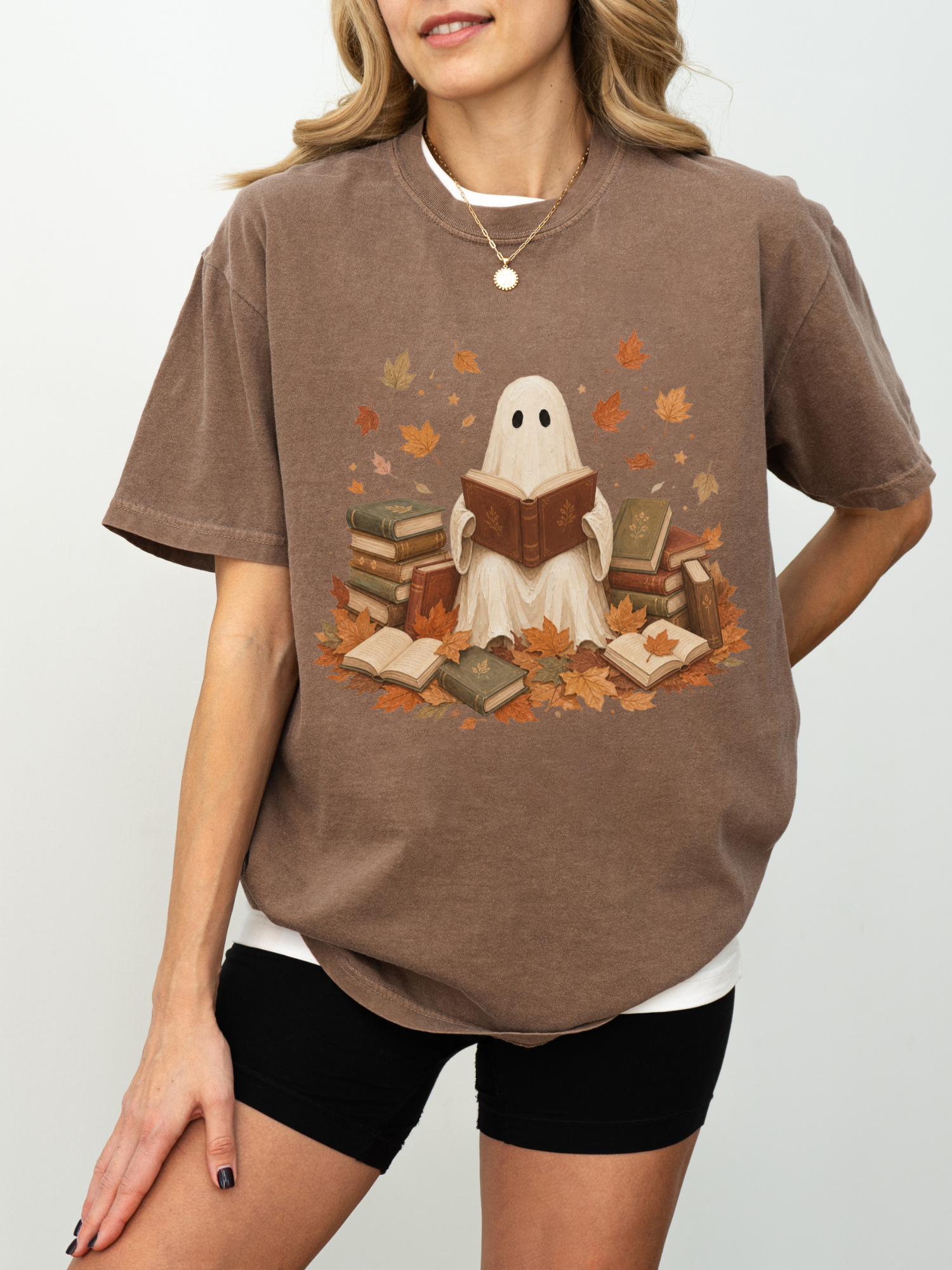 A woman wearing an espresso graphic t-shirt with a ghost reading books design, paired with black shorts, against a plain light gray background.