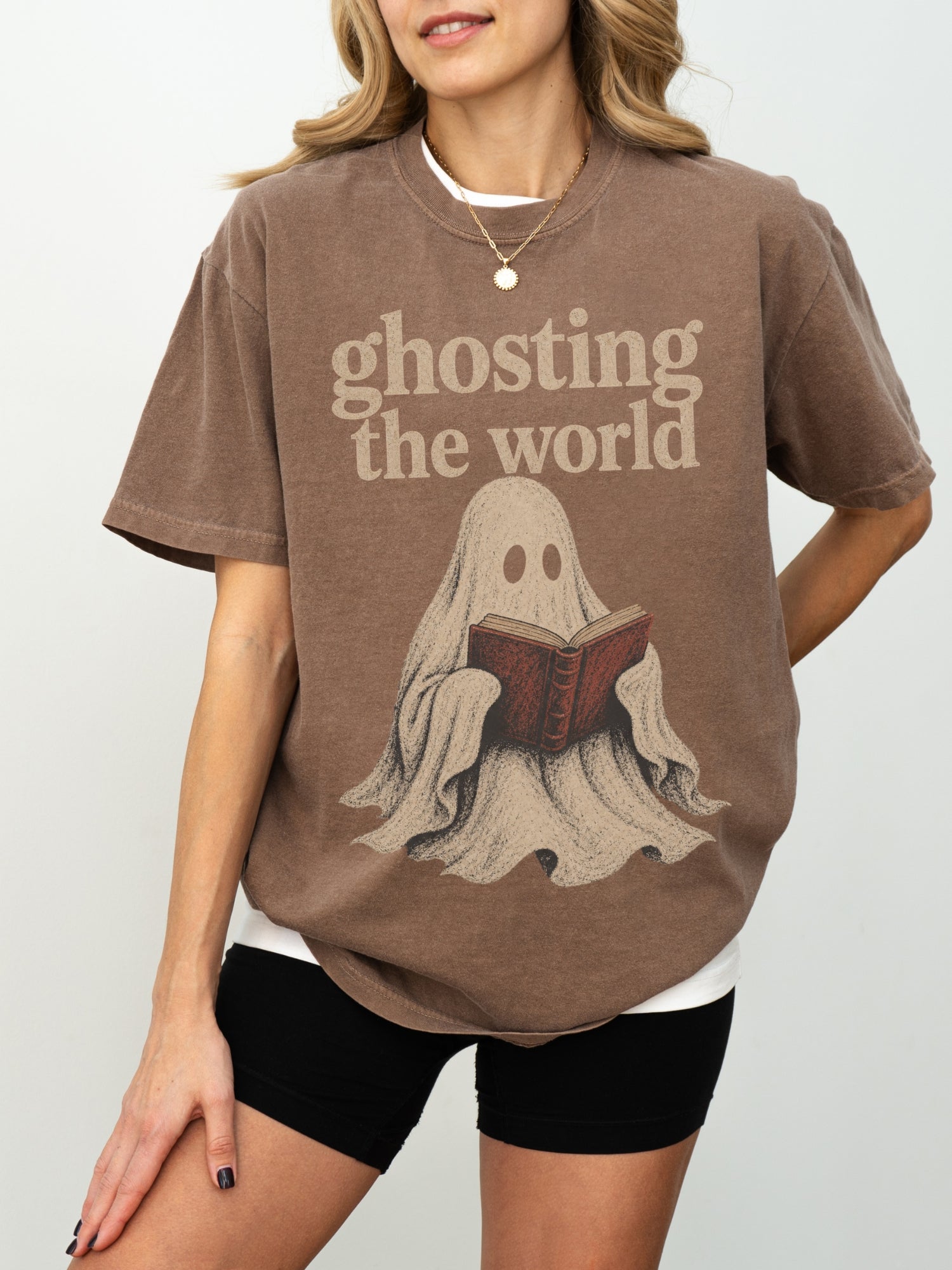 Model wearing an Espresso Comfort Colors bookish shirt with Ghosting the World text and vintage ghost reading a red book graphic