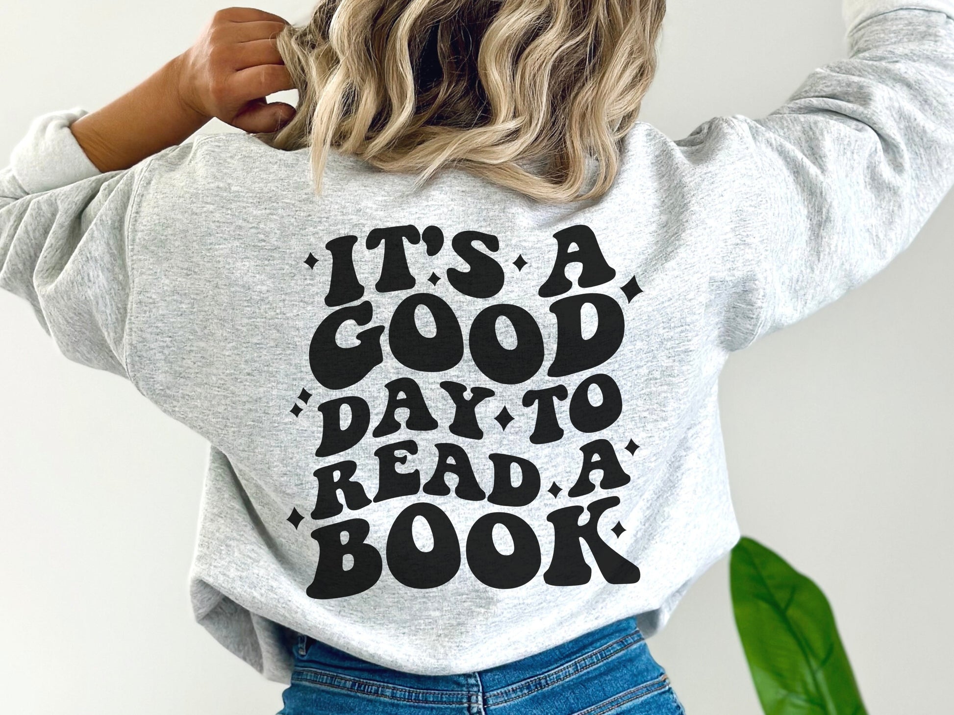 woman wearing ash grey sweatshirt with bold back print that says it's a good day to read a book