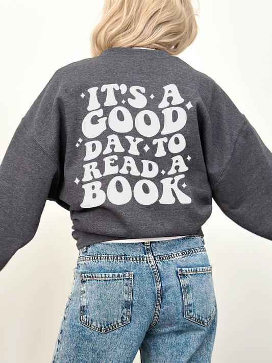 woman with blonde hair wearing dark heather sweatshirt with bold back print that says it's a good day to read a book