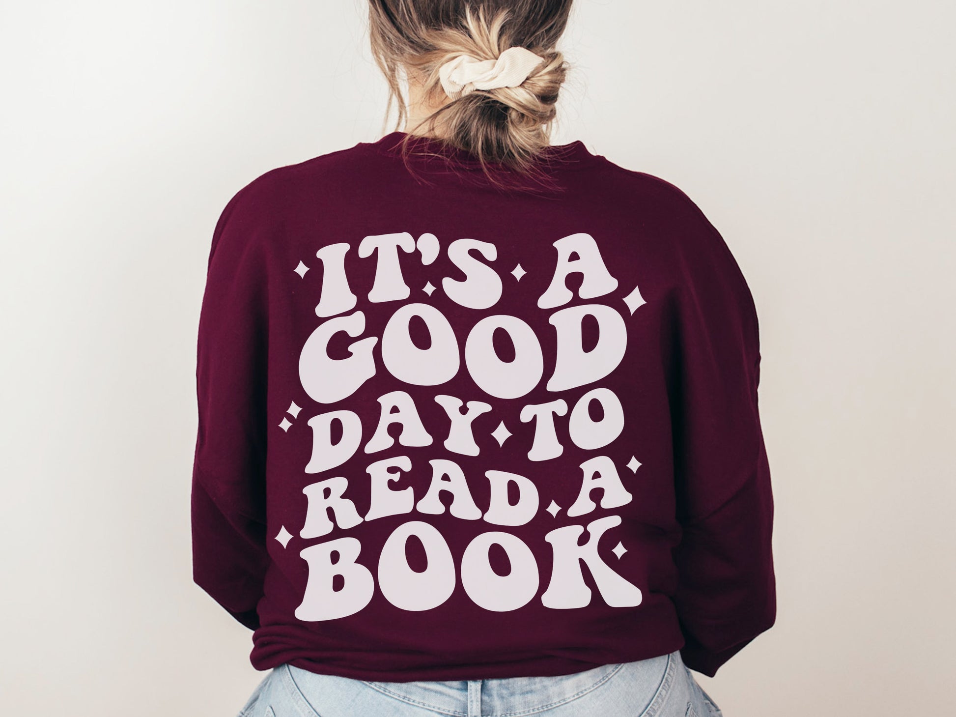 woman with scrunchie wearing maroon sweatshirt with back print that says it's a good day to read a book