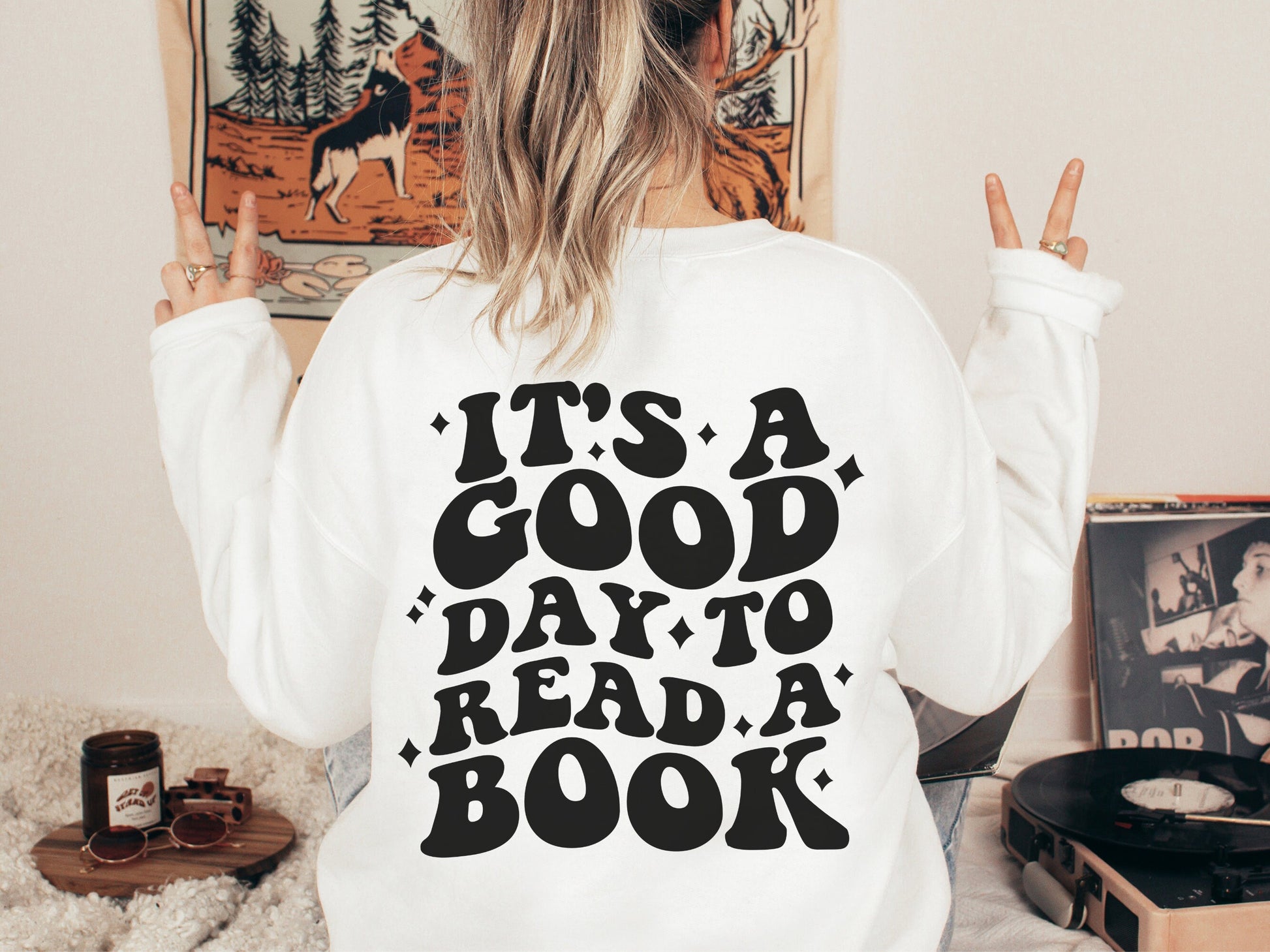 woman flashing peace signs wearing white sweatshirt with back print that says it's a good day to read a book
