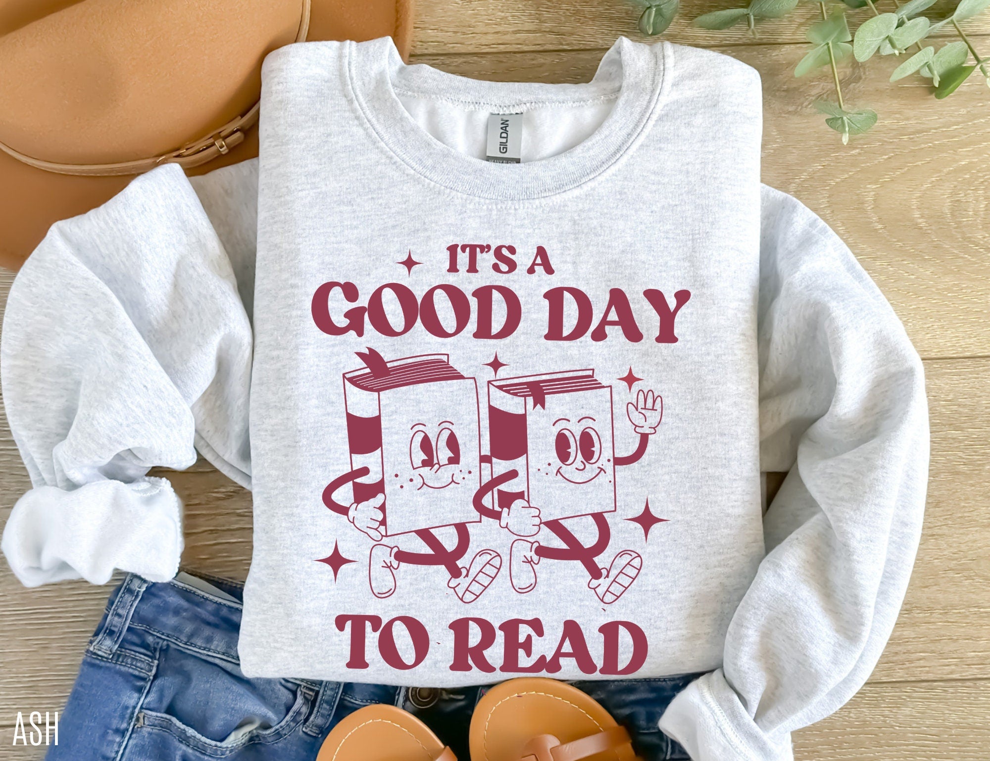 folded ash grey sweatshirt that says it's a good day to read with dancing cartoon books, styled with jeans and sandals