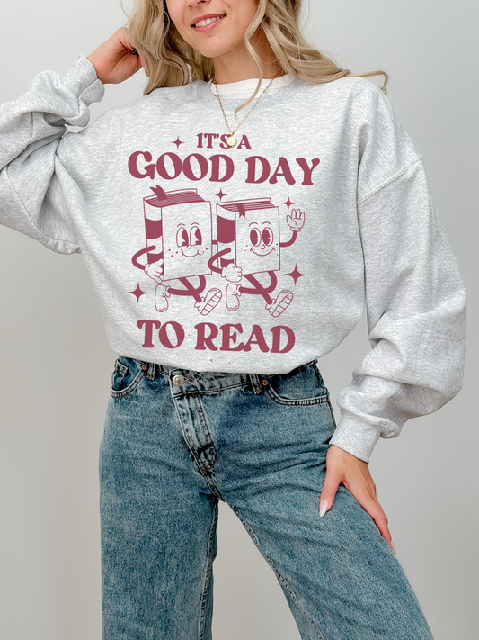woman standing in ash grey sweatshirt with it's a good day to read design and high-waisted jeans