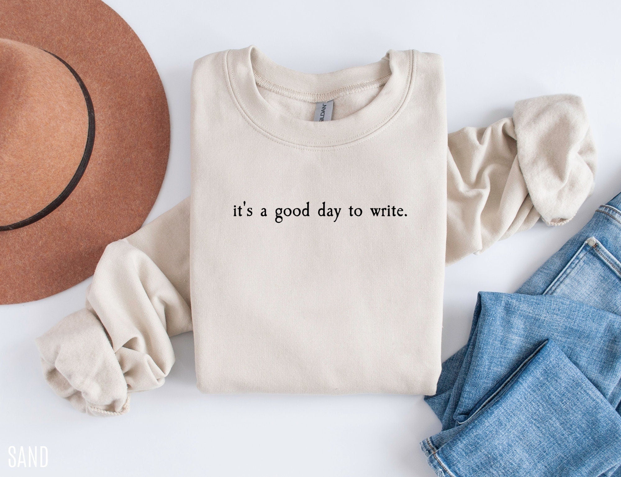 folded sand sweatshirt that says it's a good day to write styled with jeans and brown hat
