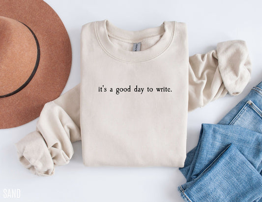 folded sand sweatshirt that says it's a good day to write styled with jeans and brown hat